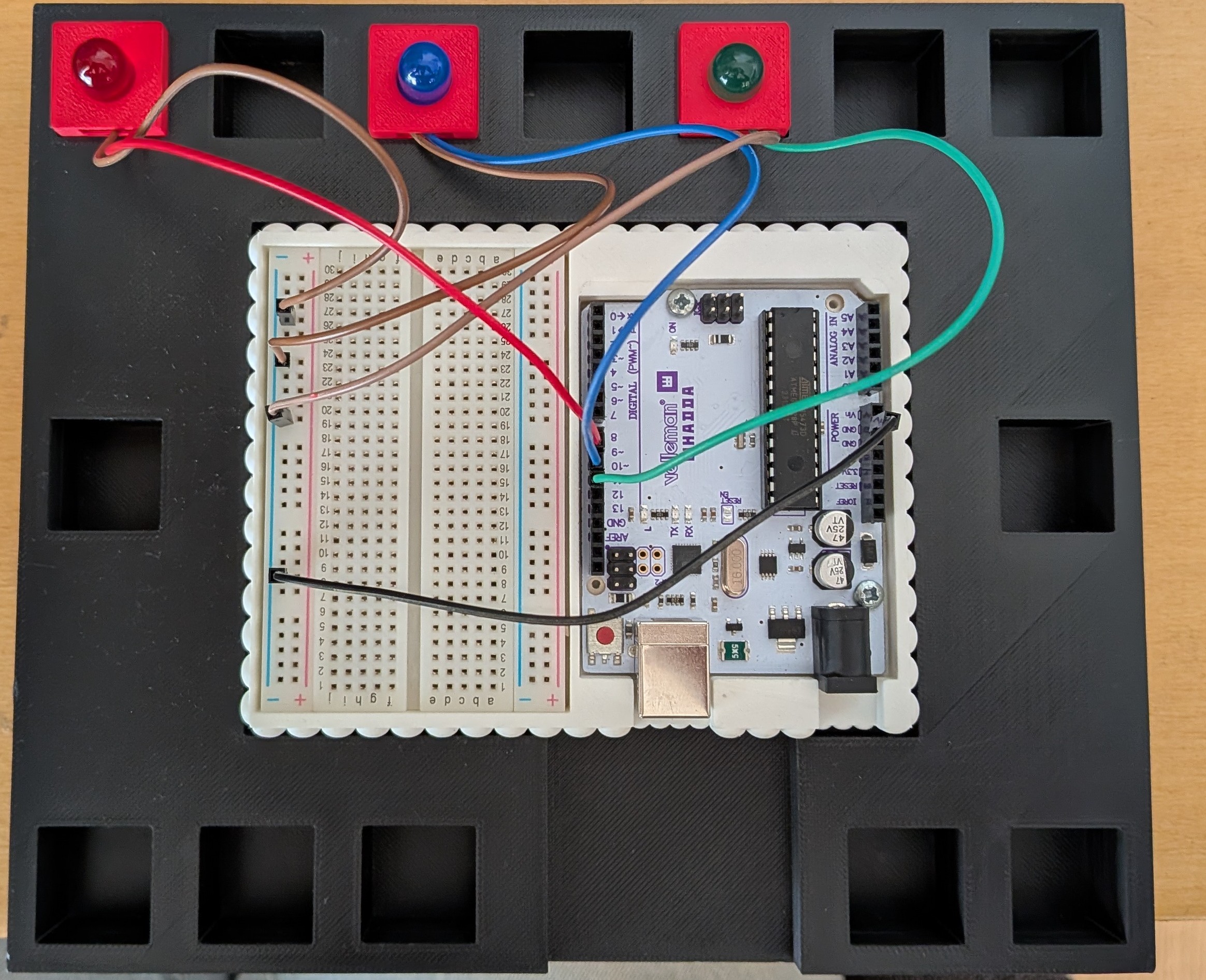 Photo du montage : trois modules LED rouge, bleu et vert, une breadboard et une carte programmable (Arduino) sur un support noir.